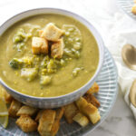 A bowl of chunky lemon broccoli soup next to three spoons.