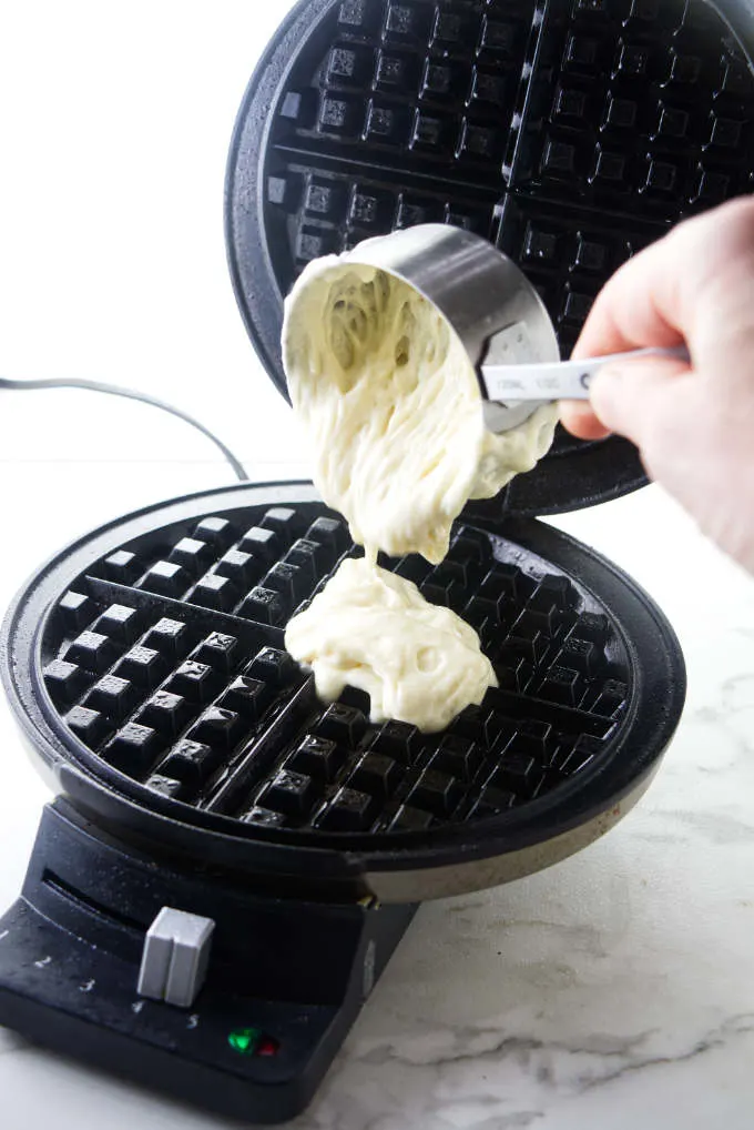Pouring waffle batter into a waffle maker.