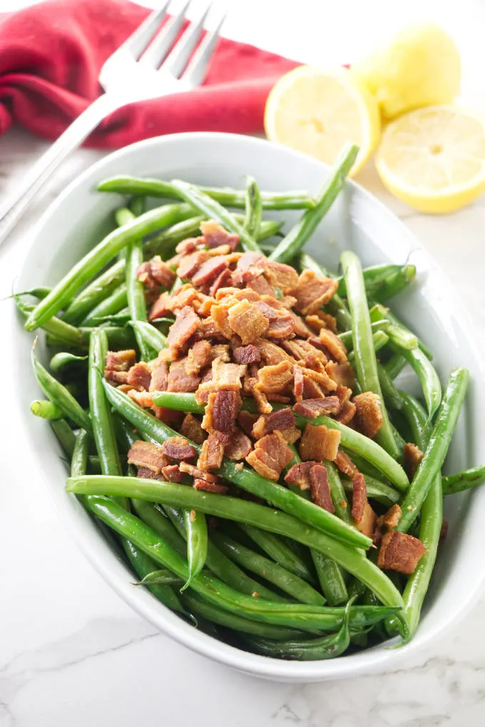 An oval serving dish filled with sauteed green beans and bacon.