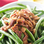 A bowl of sauteed green beans with crisp bacon on top.