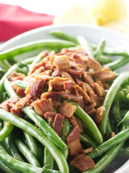 A bowl of sauteed green beans with crisp bacon on top.