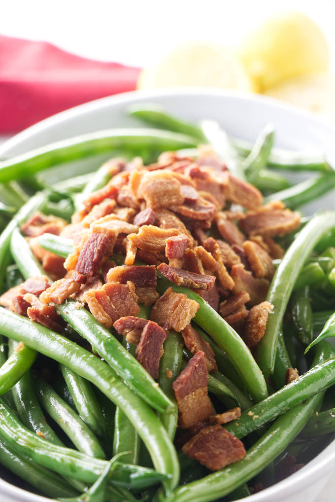 A bowl of sauteed green beans with crisp bacon on top.