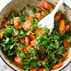 Sliced carrots in a skillet being tossed with cilantro.