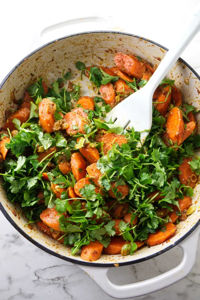 Sliced carrots in a skillet being tossed with cilantro.