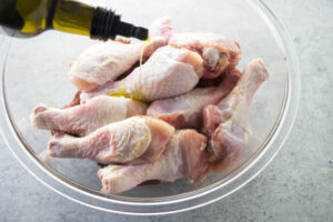 Adding olive oil to chicken drumsticks.