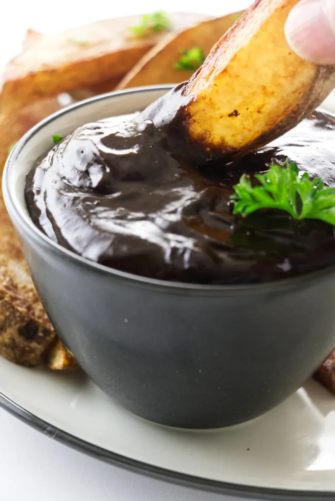 A potato wedge in a dish of black garlic aioli.