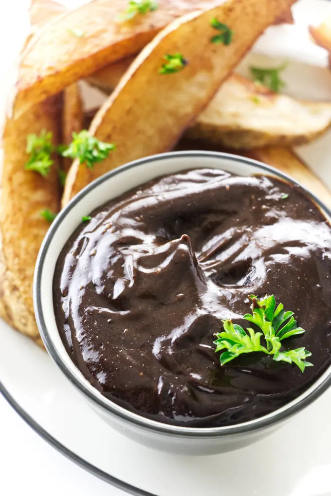 A dish of black garlic aioli next to some potato wedges.