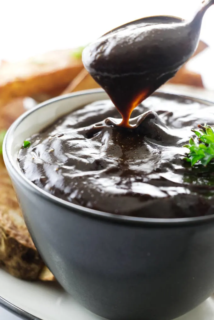 A dish of black garlic aioli with a spoon.