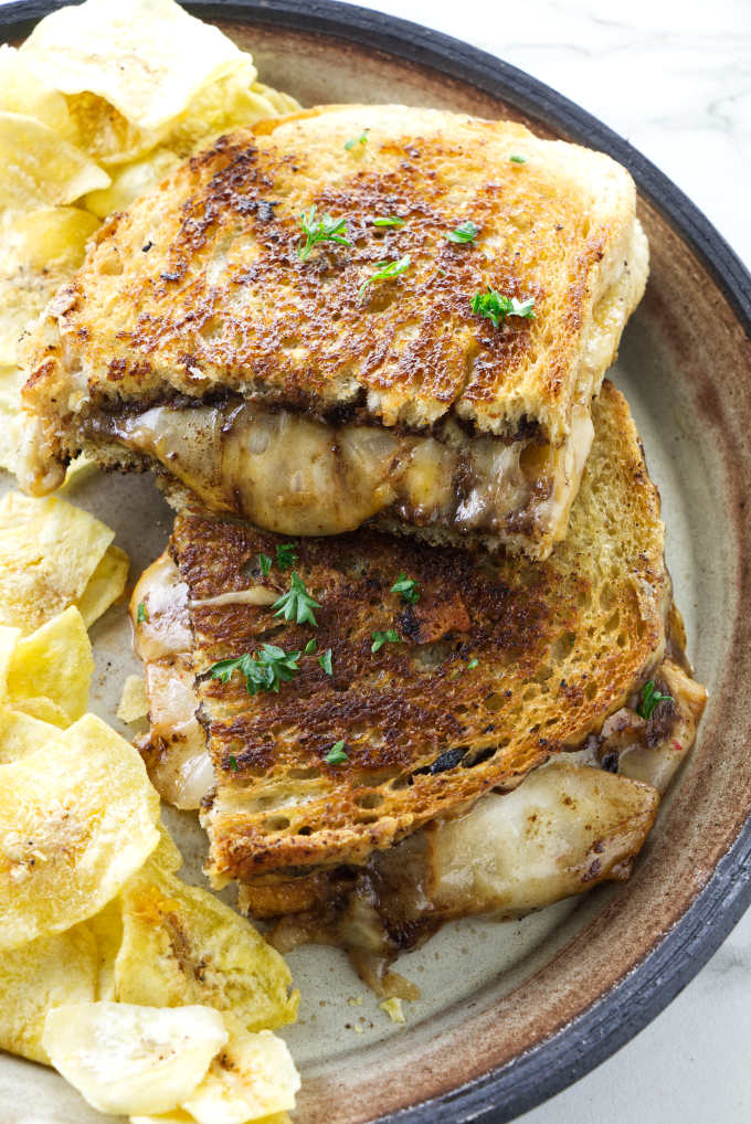 A black garlic kimchi grilled cheese sandwich on a plate with chips.