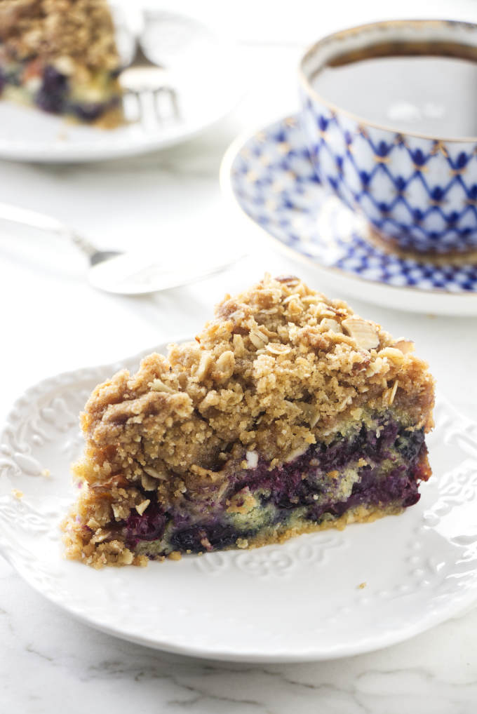 A slice of blueberry buckle cake with a cup of coffee in the background.
