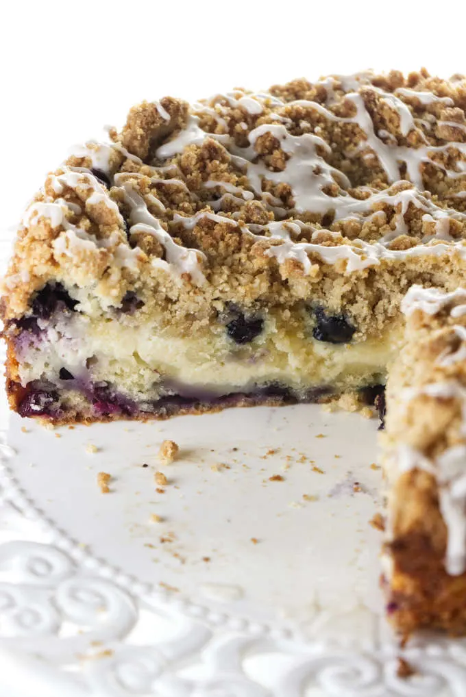 A blueberry coffee cake with a cheesecake center sliced and sitting on a cake plate.