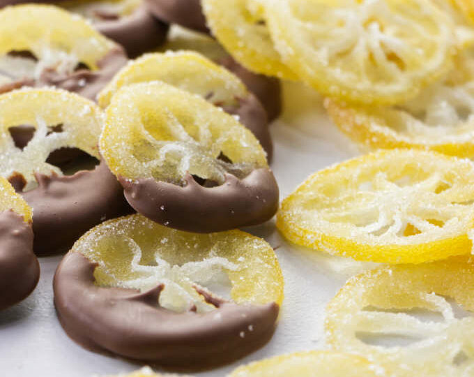 A pile of candied lemon slices coated in sugar with some of them dipped in chocolate.