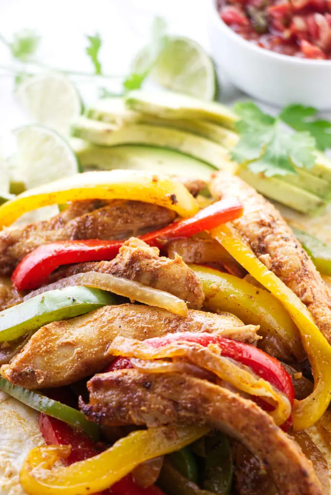 Chicken fajita mixture next to avocado and lime slices.