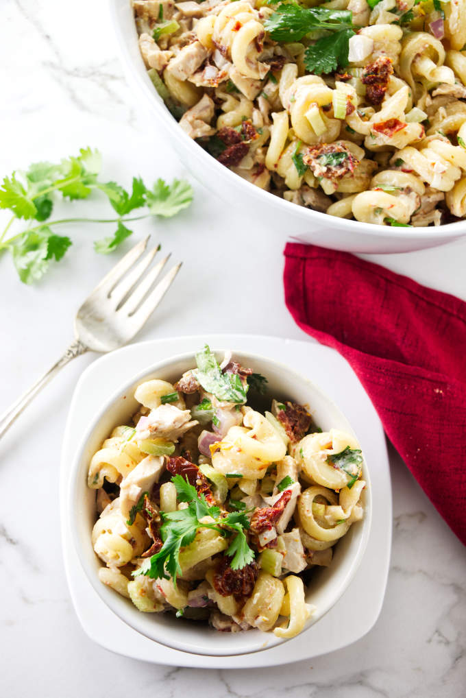 A serving bowl of pasta salad next to a pasta dish and fork.