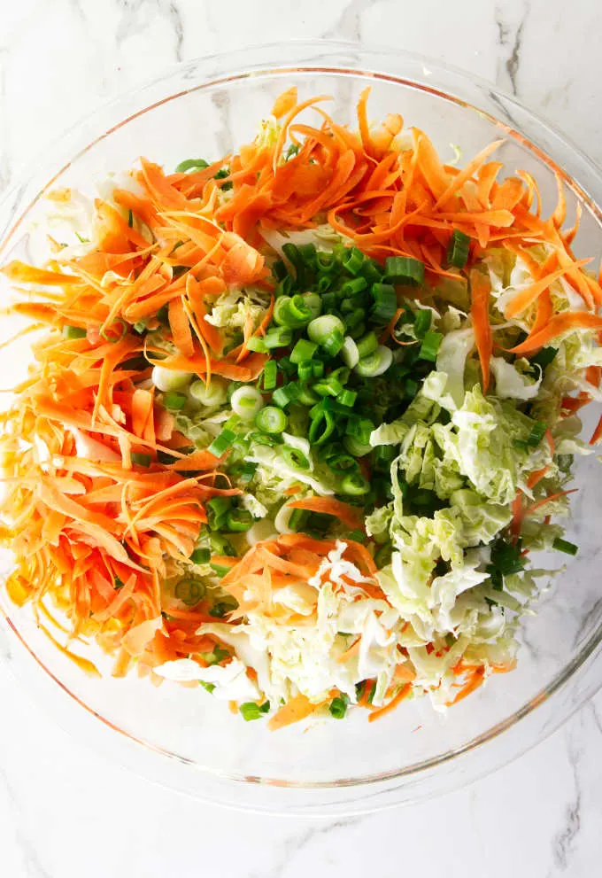 Shredded carrots, shredded cabbage and chopped green onions in a bowl.