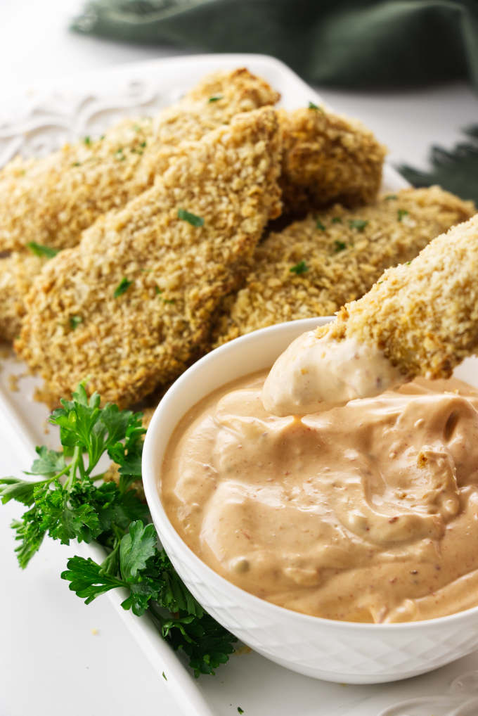 Chicken tender being dipped in a spicy chipotle aioli