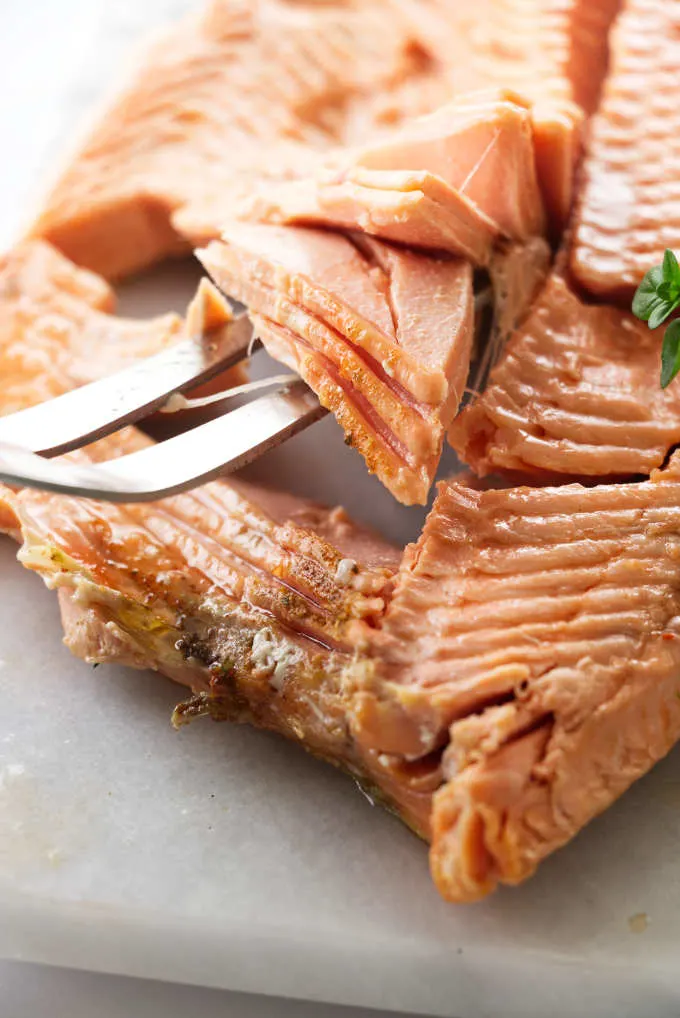 A fork lifting up on the flesh of a freshly baked whole salmon.