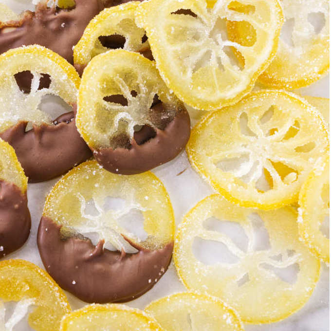 Chocolate dipped candied lemon slices next to sugar coated lemon slices.