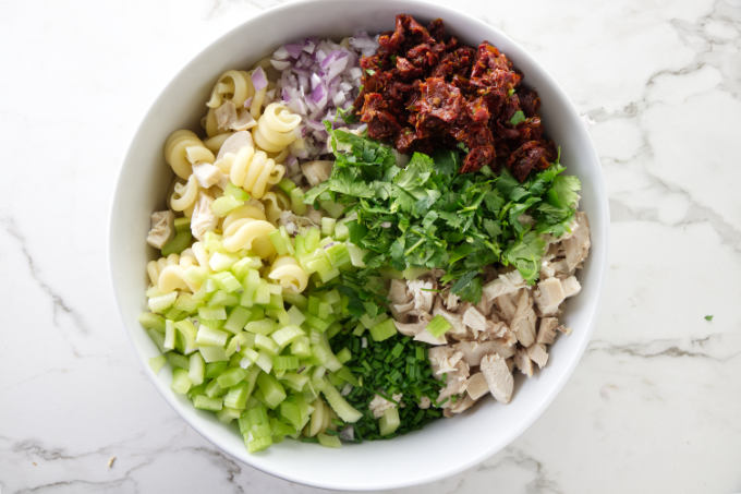 A large salad bowl filled with the ingredients for a chipotle chicken pasta salad.