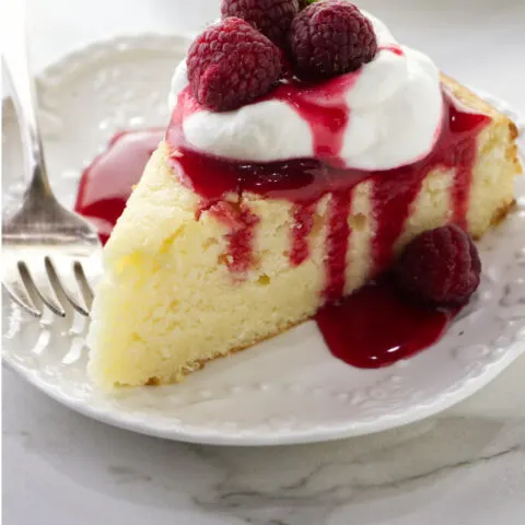 A slice of lemon ricotta cake with raspberry sauce dripping down the sides.