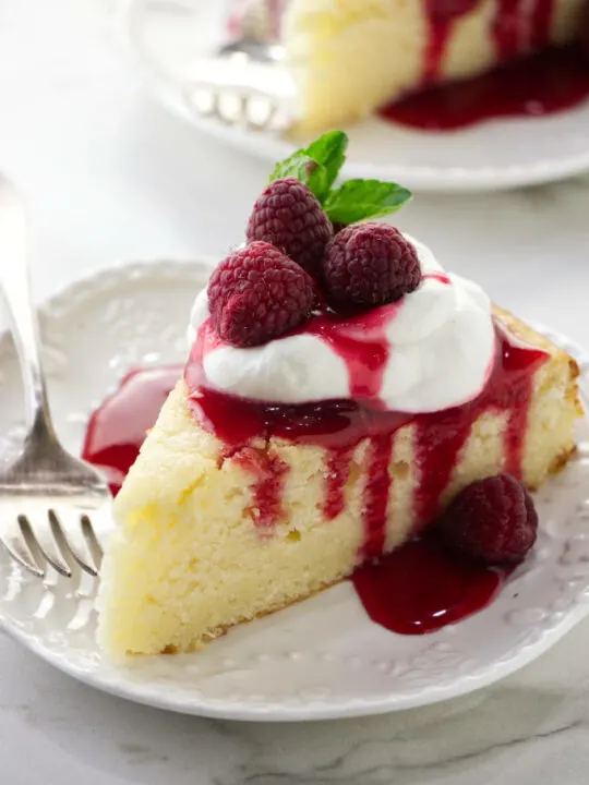 A slice of lemon ricotta cake with raspberry sauce and whipped cream on top.
