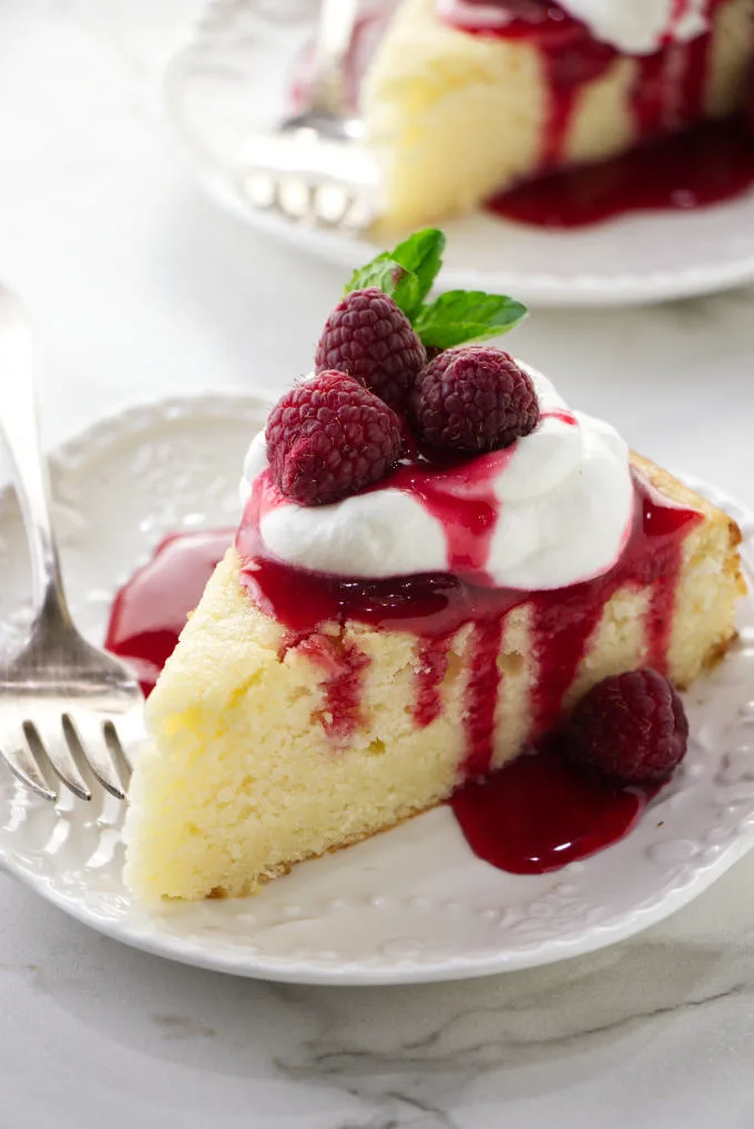 A slice of lemon ricotta cake with raspberry sauce and whipped cream on top.