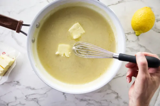 Adding butter into a pan to make lemon garlic butter sauce.