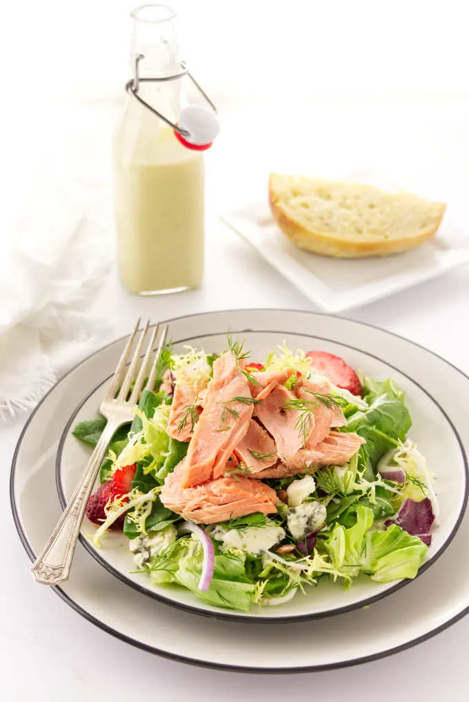 A Serving of salmon salad on a plate, preserved lemon vinaigrette and bread in the backbround