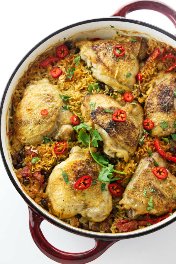 A skillet with chicken thighs on top of rice and black beans.