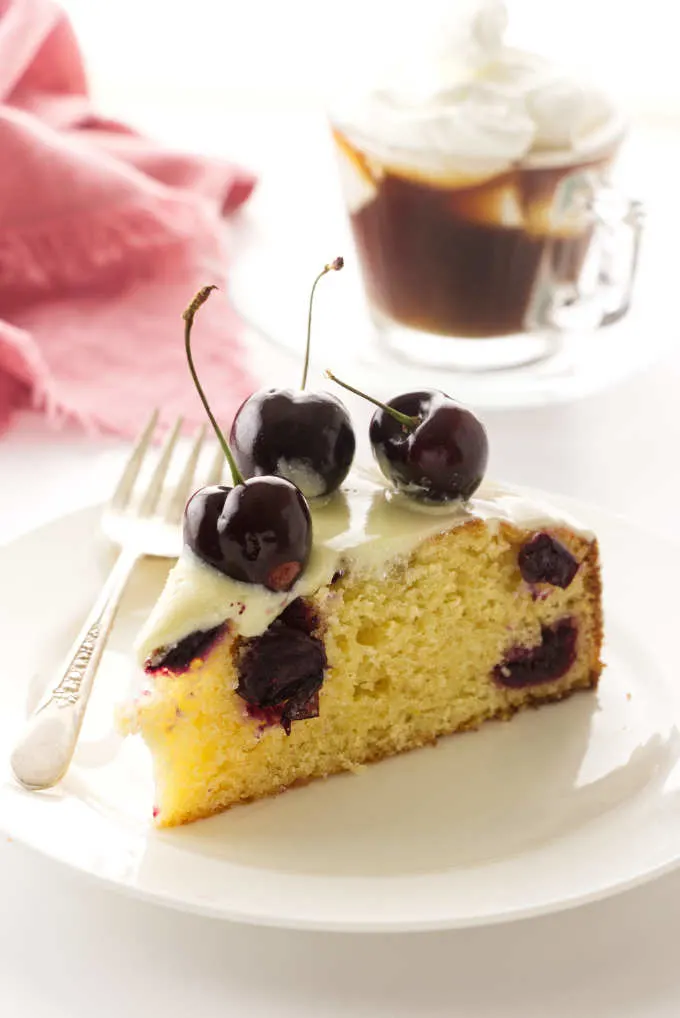 A slice of fresh cherry cake with white chocolate ganache and fresh cherries