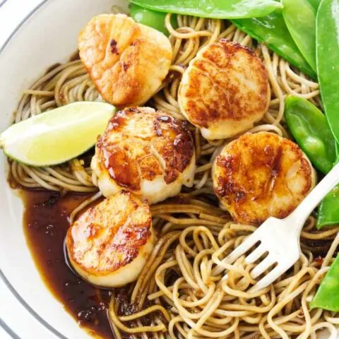 Scallops in a dish with noodles and snow peas.