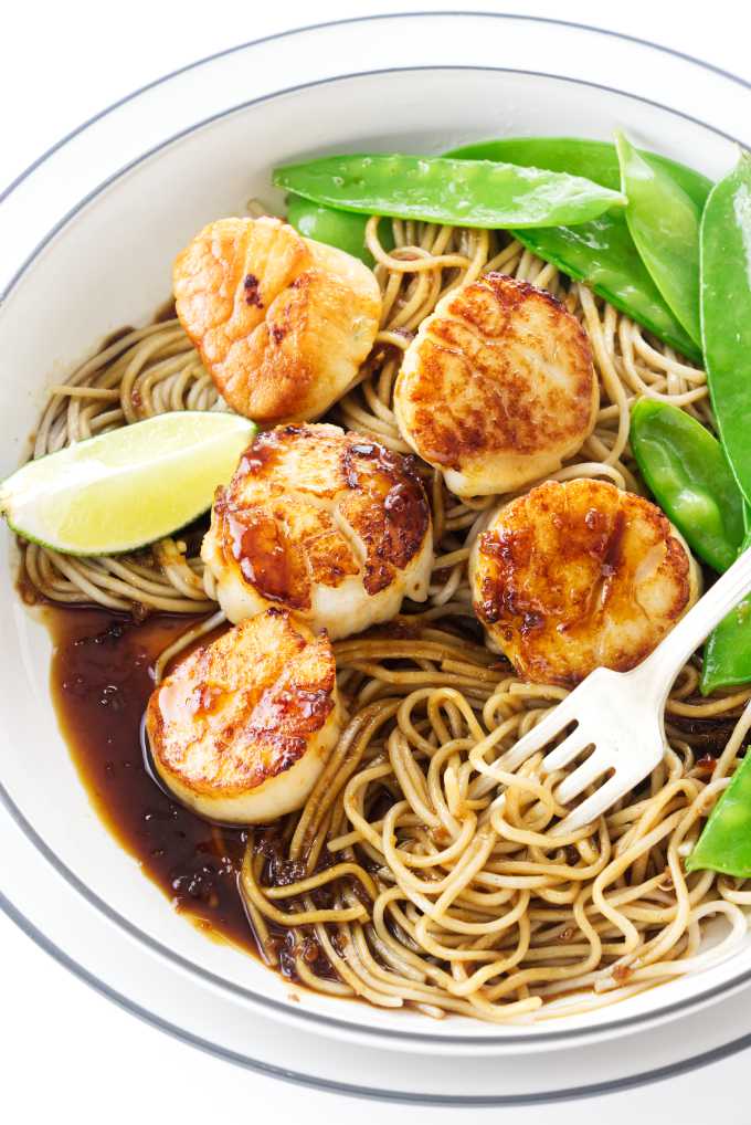 Scallops in a dish with noodles and snow peas.