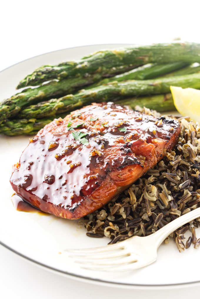 A slice of bourbon glazed salmon on a bed of rice with asparagus in the background.