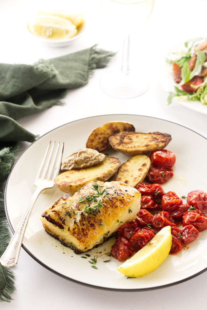 Plated Chilean Sea Bass with roasted veggies and lemon wedge