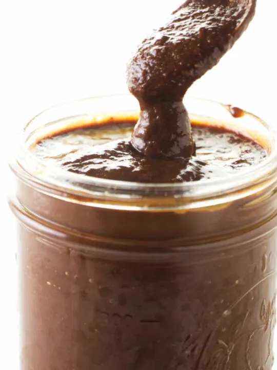 A spoon scooping out some chipotle bbq sauce from a jar.