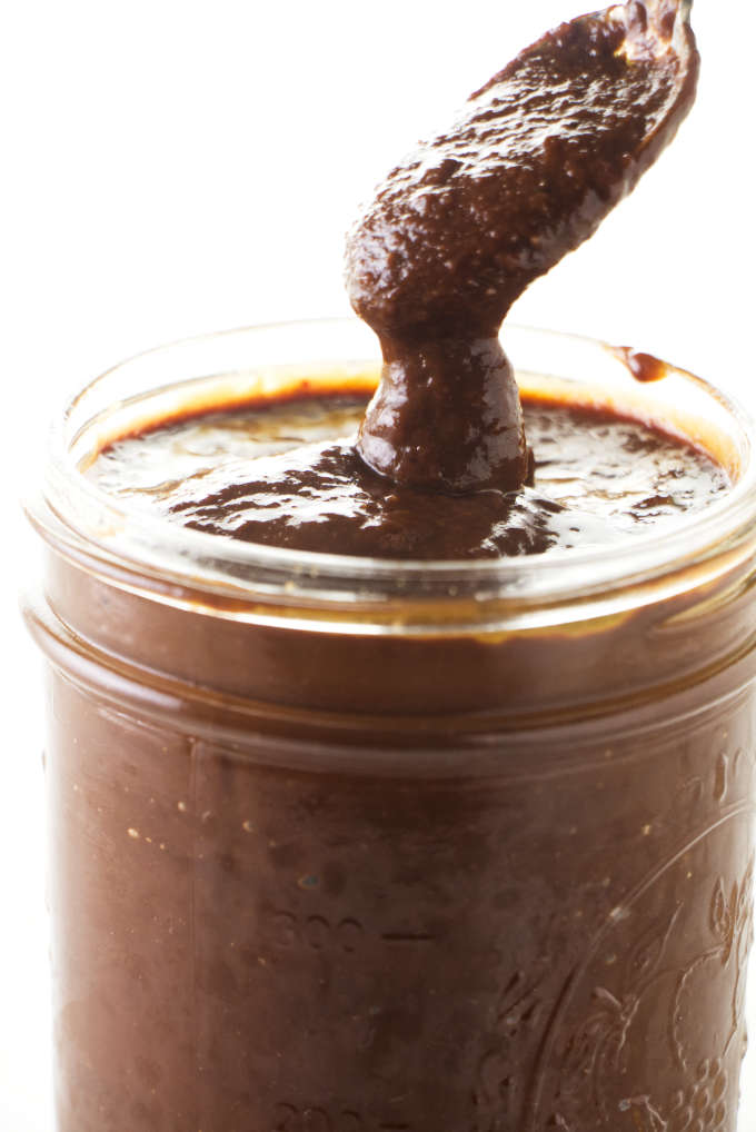 A spoon scooping out some chipotle bbq sauce from a jar.