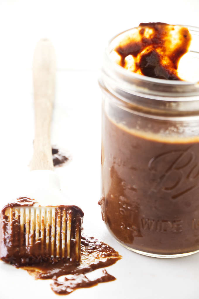 A jar of barbecue sauce next to a basting brush. 