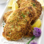 Close up view of a platter of chicken, lemon wedges and chive blossoms