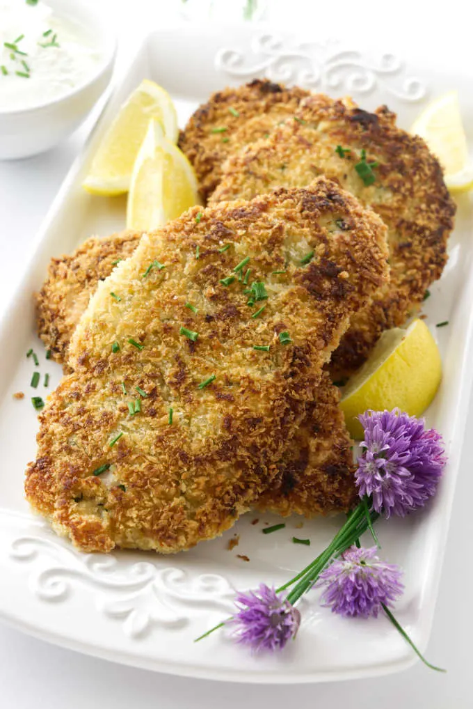 Close up view of a platter of chicken, lemon wedges and chive blossoms