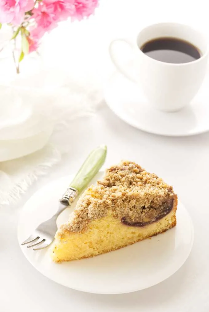 a slice of fresh fig cake on a plate, coffee, napkin and flowers in backgrond