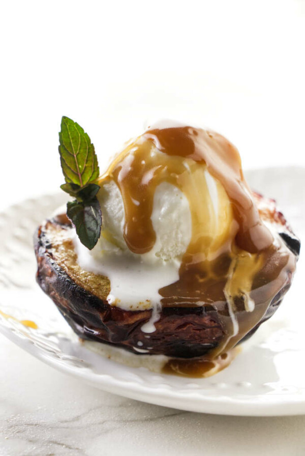 A grilled peach with ice cream and caramel sauce on top.