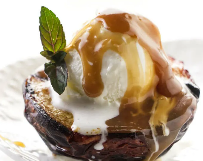 A grilled peach with ice cream and caramel sauce on top.