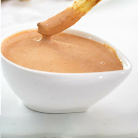 A french fry dipping into a dish of fry sauce.