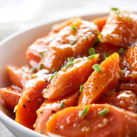 A serving dish with glazed carrots garnished with chives.