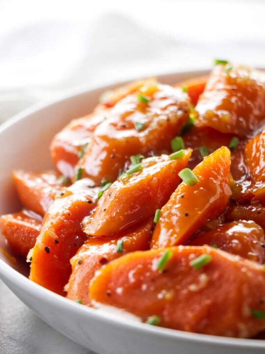 A serving dish with glazed carrots garnished with chives.