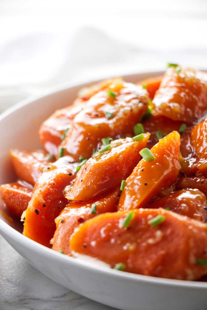 A serving dish with glazed carrots garnished with chives.