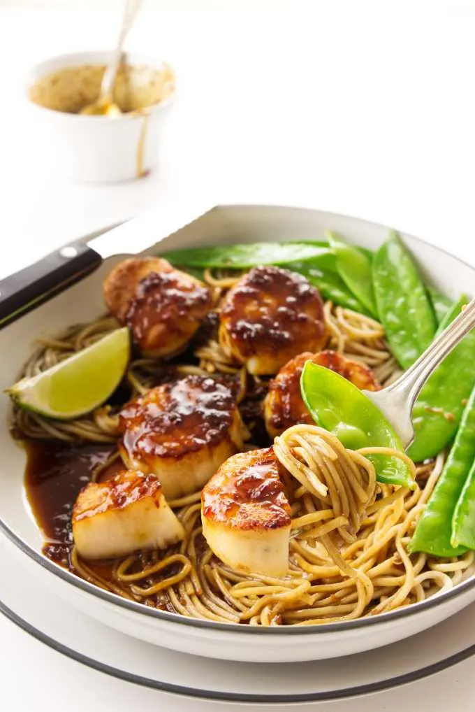 A dish of scallops with soba noodles and snow peas in an Asian style sauce.