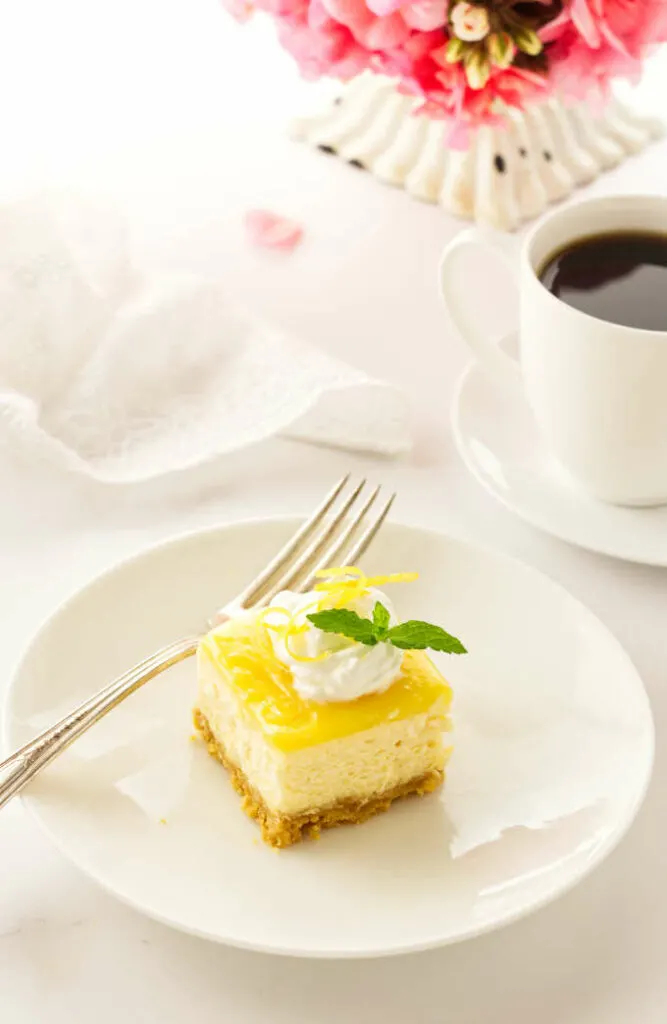 serving of cake on a plate with a fork, coffee, napkin and flowers in background