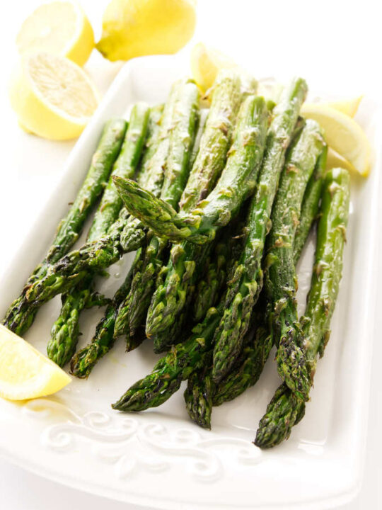 A serving platter with room temperature roasted asparagus and lemon slices.