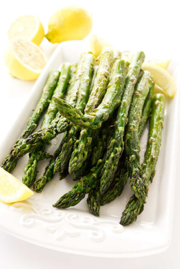 A serving platter with room temperature roasted asparagus and lemon slices.